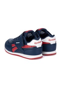 Par de zapatillas para niños Reebok en azul marino, rojo y blanco con correas de velcro, mostradas desde atrás y en un ángulo lateral sobre fondo blanco.