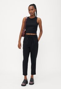 Black cropped tank top, high-waisted black trousers with drawstring, and chunky black loafers with a pink gradient sole, accessorized with a maroon bag.