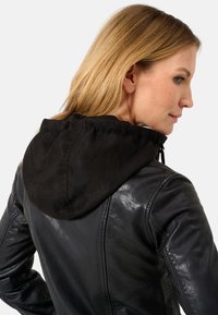 Giacca di pelle nera con una superficie liscia e un design attillato, dotata di un cappuccio in tessuto nero e di un cordoncino regolabile sul collettore.