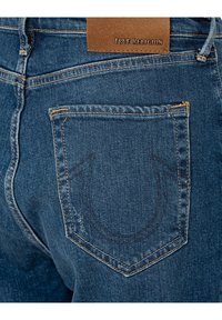 Donkerblauwe denim jeans hebben een opvallend achterzakontwerp met geborduurde stiksels en een leren label met de tekst "True Religion."