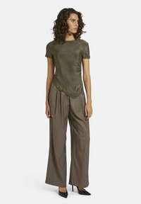 Olijfgroen top met korte mouwen en een gestructureerde afwerking, gecombineerd met losse bruine broeken en zwarte stiletto hakken. Eenvoudig, modern ontwerp.