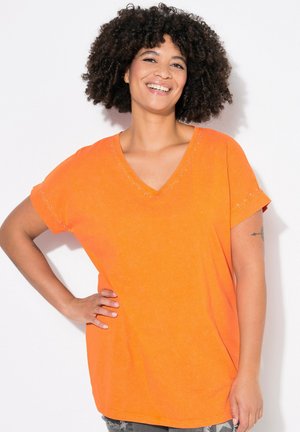 T-shirt V en orange, à manches courtes, avec des accents de clous en argent le long du décolleté et des poignets. Matériau en coton doux.