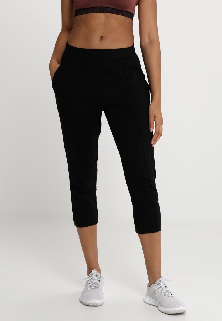 Svarta praktiska byxor med slät yta, som har sidofickor och en figurnära midja, i kombination med vita sportskor.