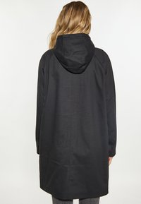 Cappotto nero con cappuccio e maniche lunghe, che arriva a metà coscia. Tessuto liscio con una vestibilità comoda, rifinito con cuciture visibili lungo le cuciture.