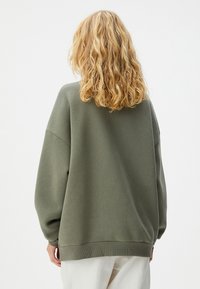 Sagegroene oversized sweatshirts met verlaagde schouders en rib gebreide boorden, gemaakt van zacht materiaal, met een eenvoudig en schoon ontwerp.
