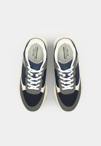 Navy and gray sneaker with textured fabric, white laces, and off-white sole. Features contrasting design elements and logo on the insole.