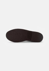Suela de un zapato marrón oscuro con un patrón texturizado y una débil marca en relieve en el centro, exhibida sobre un fondo blanco.