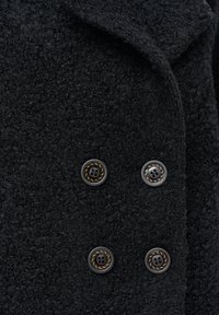 Czarny teksturowany płaszcz z grubego, plecionego materiału, ozdobiony czterema błyszczącymi guzikami z ozdobnym wzorem w postaci liny. Kołnierz jest złożony, co dodaje szczegółów.