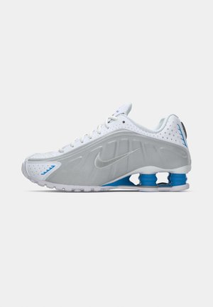 Witte sportieve schoen met grijze accenten, gestructureerd bovenwerk, perforaties voor ademend vermogen en blauwe hielveren. Heeft een platte zool.