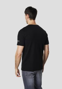 Black short-sleeve t-shirt made of cotton, featuring a round neck and a small logo detail on the left shoulder. Back view shown.
