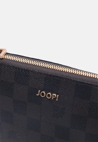 Sort tekstureret pung med guld lynlås og logo "JOOP!". Har et ternet mønster og glat læderfinish. Nærbillede.