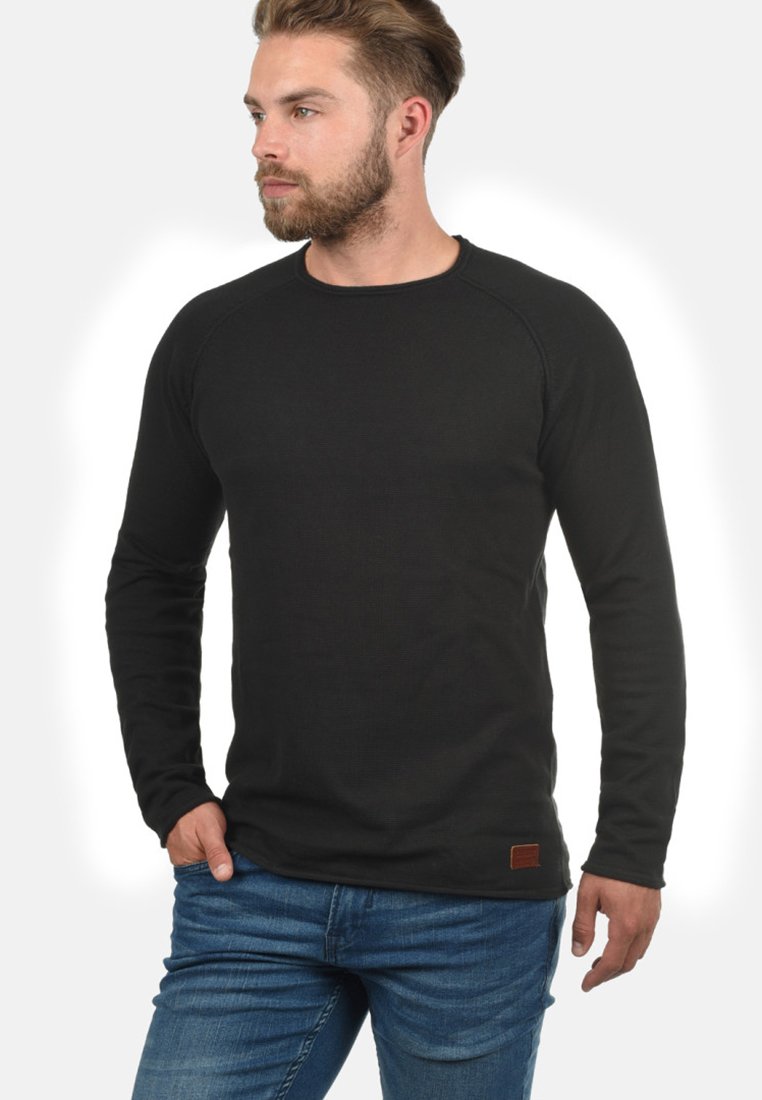 Black long-sleeve shirt with a ribbed texture, round neckline, and raglan sleeves, featuring a small brown tag at the hem.
