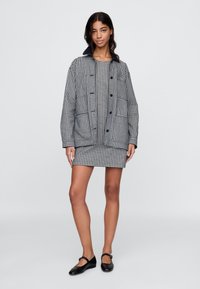 Mustvalge pionimustriga ülepaisutatud jakk sobiva, keha järgiva kleidi peal. Komplekti lõpetavad mustad baleriinikingad. Sile kangatekstuur.