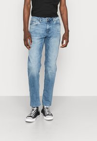 Lichtblauwe denim jeans met een rechte pijpdesign, met een klassieke vijf-pocketstijl en vage versleten patches. Gepaard met zwarte hoge sneakers.