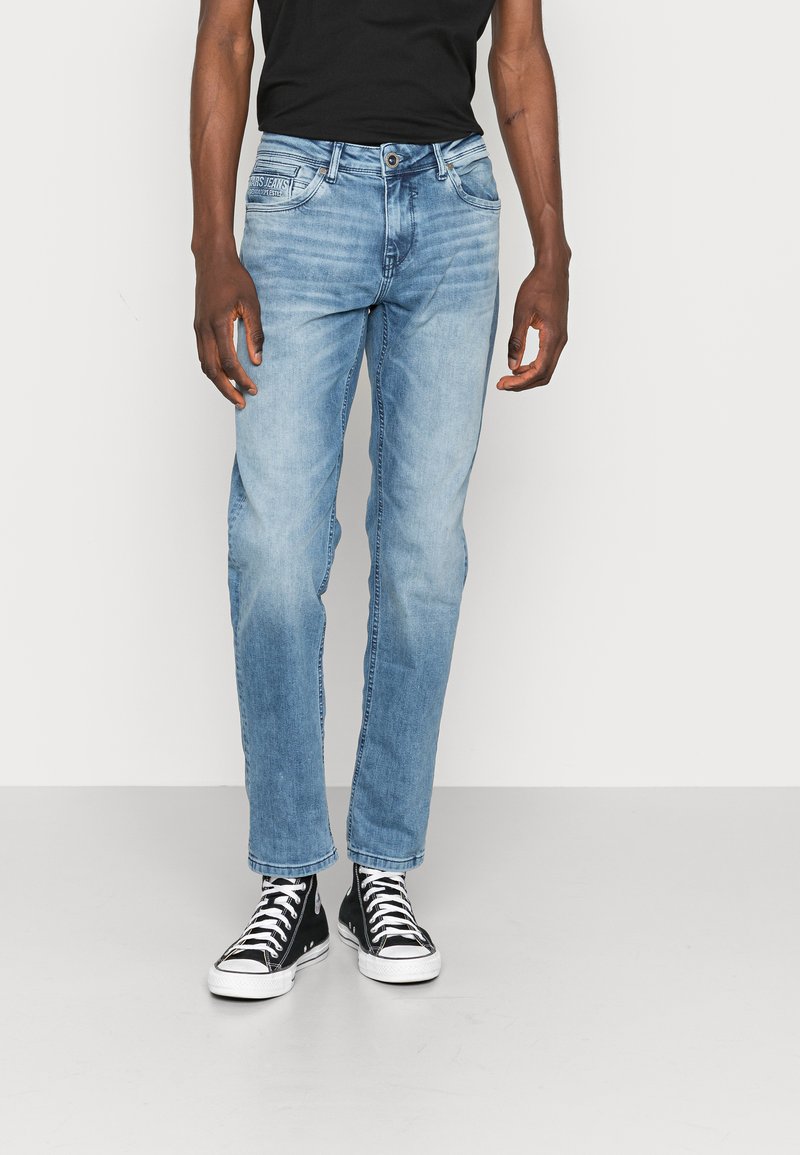 Lichtblauwe denim jeans met een rechte pijpdesign, met een klassieke vijf-pocketstijl en vage versleten patches. Gepaard met zwarte hoge sneakers.