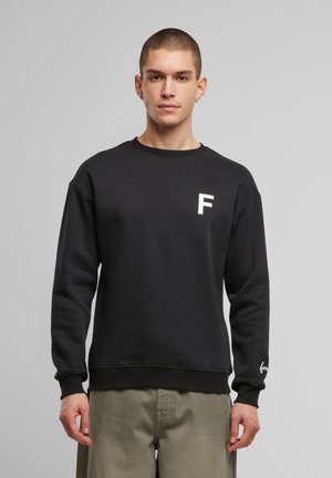 Sort sweatshirt med rund hals, prydet med et hvidt "F" logo på brystet og en mærket detalje på ærmet. Blødt, struktureret stof.