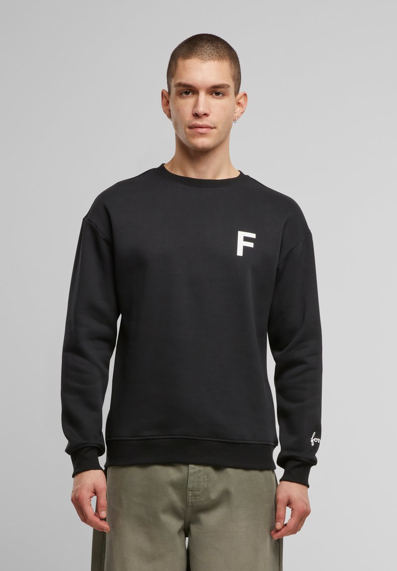 Must nääriga must kampsun, mille rinnal on valge "F" logo ja varrukal brändi aktsent. Pehme, tekstuuriga kanga.