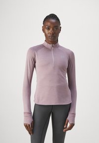 Haut à manches longues zippé en tissu lavande doux et texturé avec des manches raglan et des trous pour les pouces, associé à un legging gris ajusté.