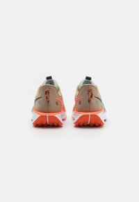 Et par beige og lys orange løbesko set fra bagsiden på en hvid overflade med teksturerede orange såler.