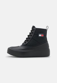Botines negros con suela de goma, upper de textil acolchado, punta redonda y diseño con cordones. Presenta un parche de logo en el lateral.