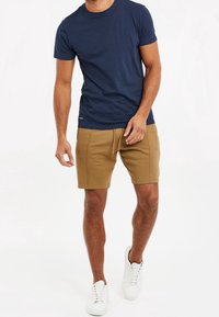 T-shirt col rond marine en coton, assorti à un short kaki. Le modèle porte des baskets blanches. Le short est doté de poches latérales et d'une coupe décontractée.