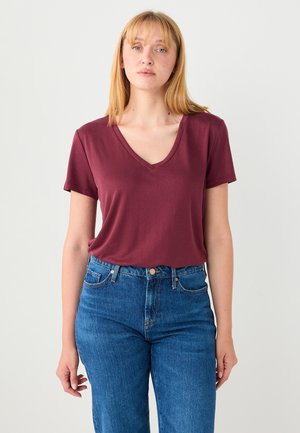 T-shirt bordeaux à col en V avec manches courtes, en tissu doux ; associé à un jean bleu taille haute. Design simple et décontracté.