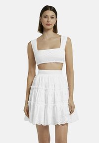 Witte two-piece outfit met een cropped top met vierkante halslijn en een gelaagde rok met geschulpte oogjes.