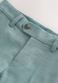 Pantalon bleu clair ajusté avec une fermeture à boutons, devant plat et passants pour ceinture, confectionné en tissu texturé avec des détails de couture subtils.