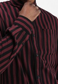 Burgundy and black striped shirt made of textured fabric; features a button-up front, collar, and single chest pocket.