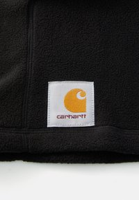 Černá fleecová tkanina s logem Carhartt na žlutém pozadí, bílém pozadí a červeným textem. Hladký povrch se sešívanými okraji.