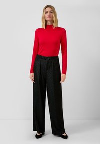 Rode lange mouw top gecombineerd met hoge taille zwarte wijdlopende broeken met een gestructureerde afwerking en een zwarte riem. Zwarte flats maken de look compleet.