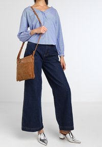 Pasiasta niebiesko-biała bluzka, szerokie ciemne dżinsy, srebrne czubate buty i brązowa skórzana torebka crossbody. Casualowy strój o miękkich fakturach.