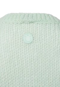 Helles mintgrünes Strickpullover mit strukturiertem Finish und einem runden, weichen Stoffpatch mit einem Smiley-Gesicht auf der Rückseite.