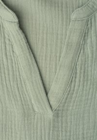 Tissu vert clair texturé avec un décolleté en V et un large col en matière tissée douce et respirante.