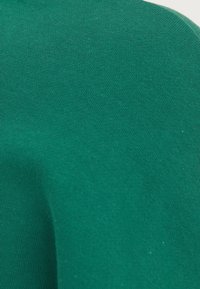 Tela de algodón verde que muestra una textura suave con patrones de punto uniformes, con un ligero caído y sin herrajes o acentos distintivos.