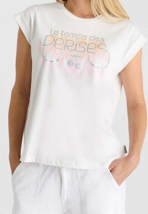 Frau trägt ein weißes ärmelloses T-Shirt mit aufgekrempelten Ärmeln und einem bunten "Le temps des cerises"-Logo auf der Brust.