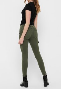 Olivgröna cargobyxor med slim fit, med bakfickor och sidofickor, kombinerade med en svart t-shirt med kort ärm och klackstövlar.