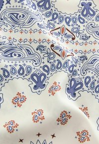 Fabric with intricate paisley and floral patterns in blue, brown, and beige on a white background, showing slight folds.