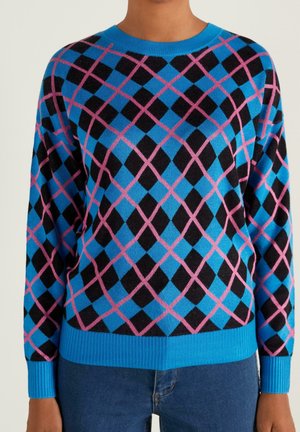 Pull bleu avec motif losanges argyle noir et rose, porté avec un jean bleu, montré du cou aux hanches.