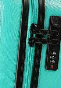 Maleta rígida en color turquesa con un acabado texturizado, tiradores de cremallera negros dobles y una cerradura de combinación integrada para mayor seguridad.