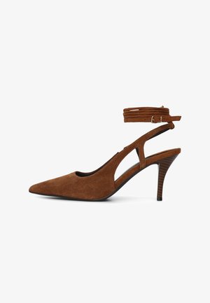 Scarpa con tacco alto in camoscio marrone, punta a punta, cinturino alla caviglia e design con ritagli. Presenta un tacco lavorato e una silhouette elegante.