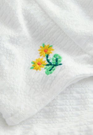 Witte handdoek van gemêleerde stof met gele geborduurde bloemen en groene bladeren in één hoek, wat een decoratieve toets toevoegt.