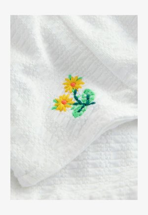 Bílý ručník se strukturální tkaninou a žlutými vyšívanými květinami a zelenými listy v jednom rohu, který přidává dekorativní prvek.
