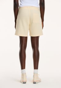 Yellow textured knit shorts with a back pocket, featuring a relaxed fit and visible side stitching, paired with beige high-top sneakers.