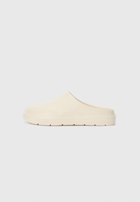 Beige slip-on clogs with a smooth, matte finish. Rounded toe, low heel, and textured sole. Minimalist design with no visible hardware.