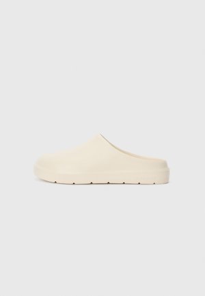 Beige slip-on clogs with a smooth, matte finish. Rounded toe, low heel, and textured sole. Minimalist design with no visible hardware.