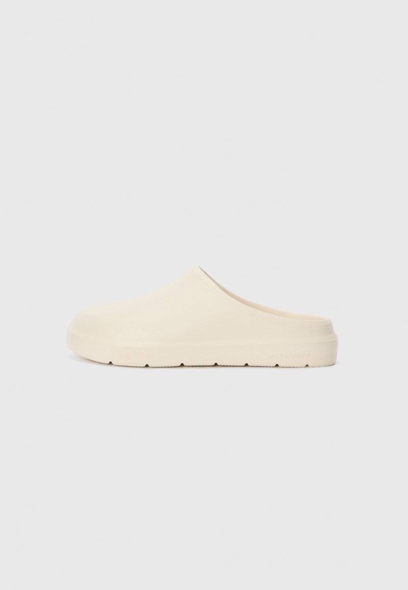 Beige slip-on clogs with a smooth, matte finish. Rounded toe, low heel, and textured sole. Minimalist design with no visible hardware.
