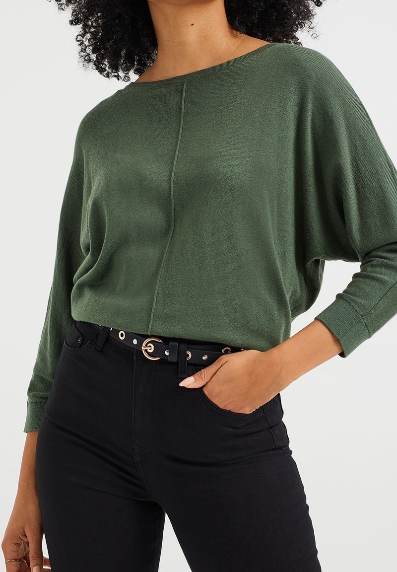 Luźny, zielony sweter dzianinowy z szerokim dekoltem i opuszczonymi ramionami, w połączeniu z czarnymi spodniami o wysokim stanue i czarnym paskiem ze złotymi elementami.