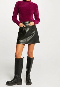 Futrzasty purpurowy sweter z wysokim kołnierzem, zestawiony z czarną skórzaną mini spódnicą z dwoma przednimi kieszeniami oraz czarnymi skórzanymi kozakiami za kolano.