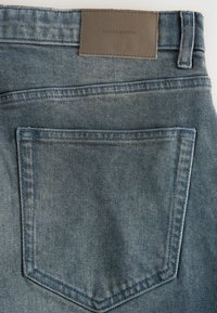 Jeans aus Denim mit einem hellblauen Waschung, ausgestattet mit einer Gesäßtasche, einem Lederetikett mit der Aufschrift "DENIM SUPPLY" und sichtbaren Nähdetails.